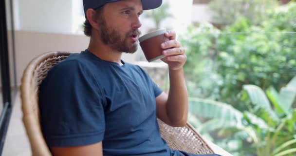 Mies sinisissä vaatteissa juo kahvia sumeilla lehdillä taustana — kuvapankkivideo