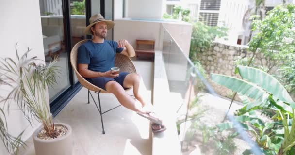 Hombre sentado en silla de caña en el balcón con paneles de vidrio — Vídeo de stock
