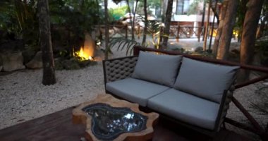 Tropikal ağaçlar ve bitkilerle çevrili rahat kanepe ve cam sehpa.