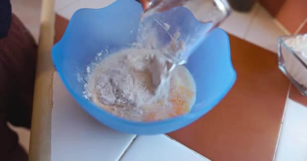 Людина поливає борошно в синю миску з яйцями і молоком — стокове відео