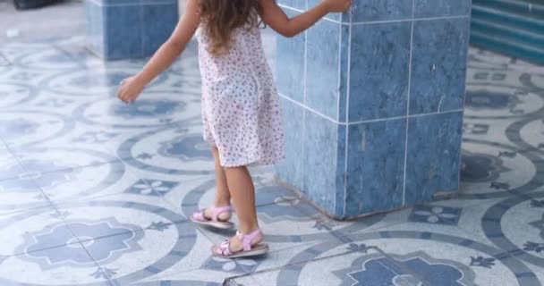 Schattig klein meisje struikelen terwijl speels rondrennen blauw betegelde kolom — Stockvideo