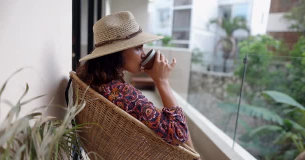 Beautiful woman drinking coffee and sitting on cane chair on balcony — Stock Video