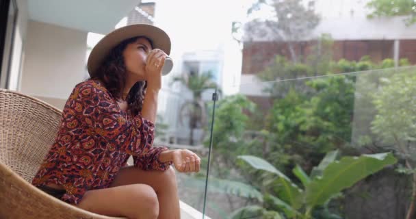 Mooie vrouw drinken van koffie en zitten op riet stoel op balkon — Stockvideo
