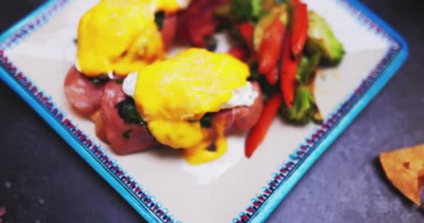 Plate of delicious eggs benedict and roasted vegetables on black surface — Stock Video