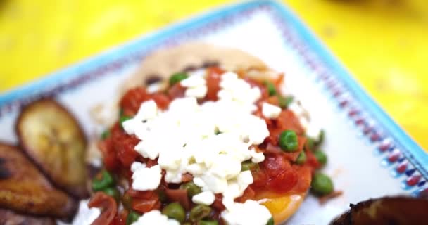 Bir tabak huevos rancheros ve sarı yüzeyde kızarmış muz dilimleri. — Stok video