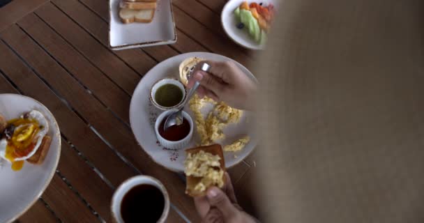 Mãos femininas adicionando molho à torrada com ovos mexidos acima da mesa de madeira — Vídeo de Stock
