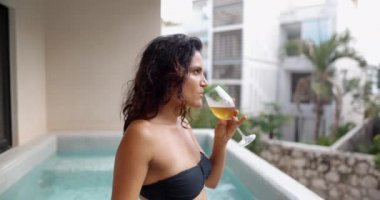 Güzel esmer kadın havuzda şampanya içiyor.