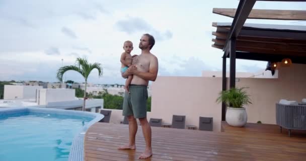 Barbudo hombre llevando lindo niño en piscina bajo cielo nublado — Vídeos de Stock