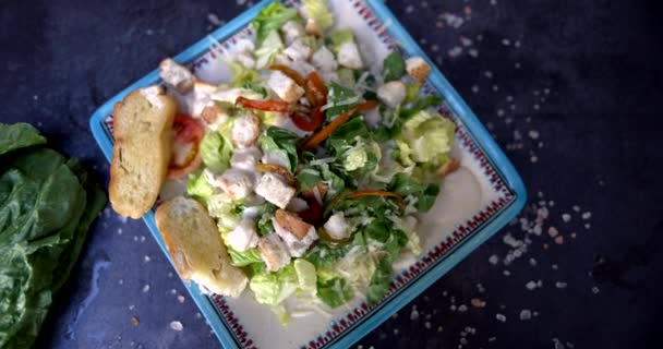 Tallrik med läcker sallad omgiven av grönsaker och salt på svart yta — Stockvideo