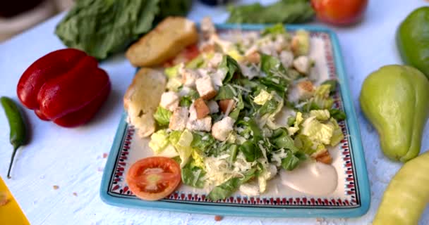 Тарілка смачного салату в оточенні овочів на білій поверхні — стокове відео
