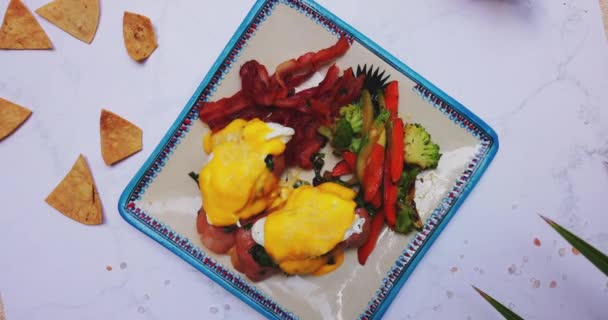 Plate of delicious eggs benedict and roasted vegetables on white surface — Stock Video