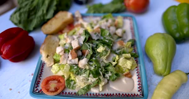 Тарілка смачного салату в оточенні овочів на білій поверхні — стокове відео
