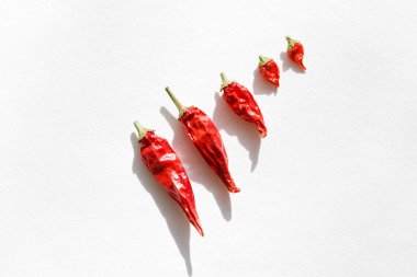 Kırmızı biber. Chili biberi. Acı biber kabukları beyaz arka planda bir sırada büyükten küçüğe uzanır. Üst görünüm