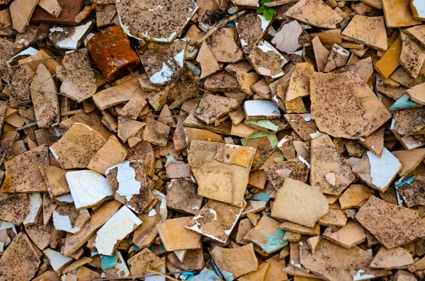 Background of broken tiles and rusty pipe detail. Light beige and white broken tiles lay on the ground. A pileup of broken ceramic tiles due to improper residential construction material. Can be use