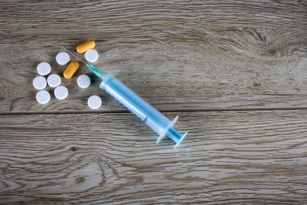 Syringe and pills on wooden board — Stock Photo, Image