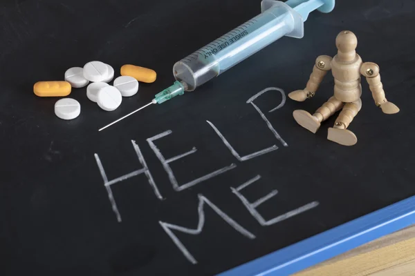 Syringe, pills and wooden human figure on chalkboard with help me — Stock Photo, Image