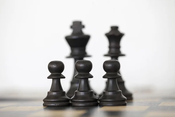 Rey negro de madera y piezas de ajedrez reina detrás de peones —  Fotos de Stock