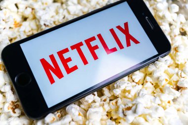 Uzhhorod, Ukrayna. 19 Ekim 2021 Bir adam Netflix 'te film izliyor. İnternet servisi. akıllı telefon beyaz görüntü netflix telefon patlamış mısır üzerine uzanır. 