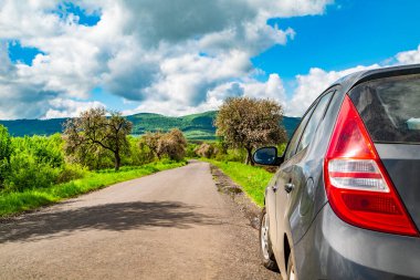 Yolun kenarındaki bir araba, arka plandaki bahar ağaçlarına karşı dağların arkası. Seyahat kavramı.