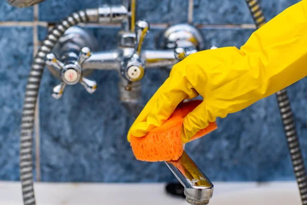 Hizmetçinin eli ya da temizlikçi kadın banyoda yeni bir lavabo temizler, su musluğunu sarı eldivenler ve yeşil bir süngerle temizler.. 
