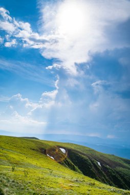 Güzel dağ manzarası. Çimenlerle kaplı dağlar, güneşte mavi gökyüzü bulutları. Doğanın dikey fotoğrafı. Temiz hava kavramı. 