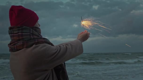 Mujer en la costa del océano con chispas de fuegos artificiales — Vídeos de Stock