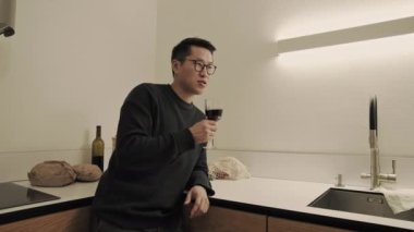 Asian man drinks wine in kitchen