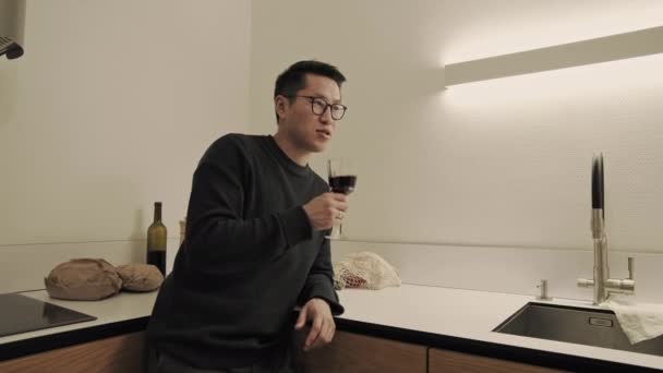 Asian man drinks wine in kitchen — Vídeos de Stock