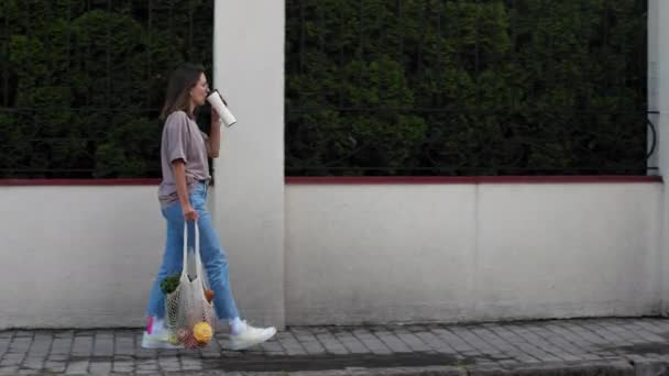 Vrouw wandelingen in de stad met mesh string gebreide boodschappentas — Stockvideo