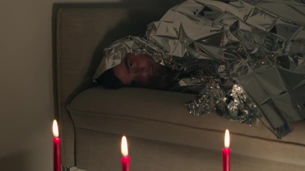 Man bedekt met een folie deken op zoek naar kaarsen — Stockvideo