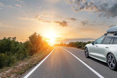 Araba yol boyunca gidiyor. Gri bir araba banliyö otoyolunda Gün batımında ya da şafakta.