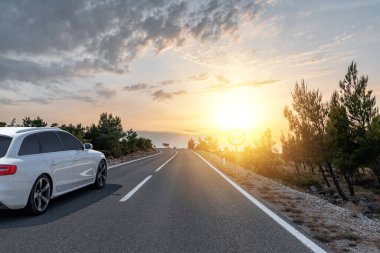 Araba yol boyunca gidiyor. Gri bir araba banliyö otoyolunda Gün batımında ya da şafakta.