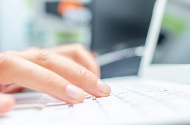 Bir kadın beyaz bir dizüstü bilgisayarda klavye kullanıyor..