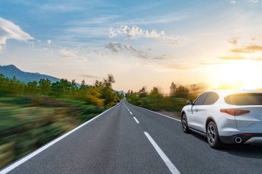 Güneşli bir yaz gününde güzel bir yolda beyaz bir araba sürüyor..