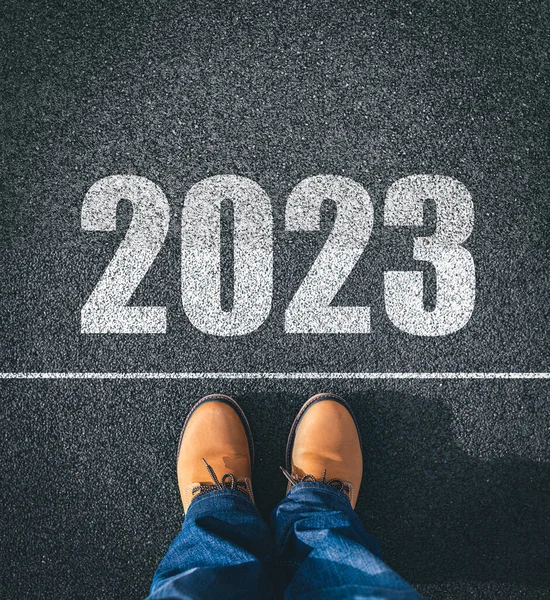 New year 2023, concept. 2023 inscription on the asphalt. The man in boots takes a step into the new year 2023.