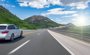 Güneşli bir yaz gününde güzel bir yolda beyaz bir araba sürüyor..