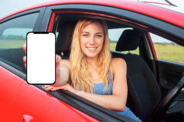 A young woman in a car shows a smartphone with a white screen.