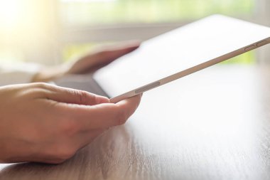 Digital tablet computer with a blank screen in the hands on wooden table