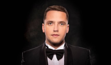Portrait of a man in a tuxedo on a dark background.