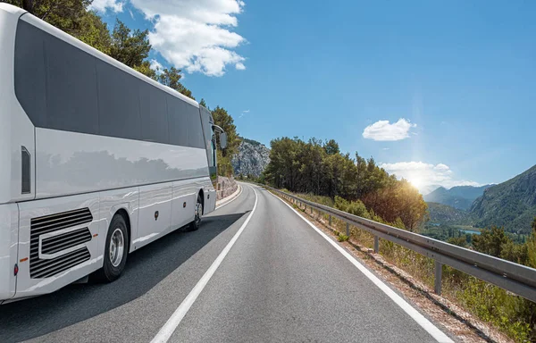 A white tourist bus rides along the highway against the backdrop of a beautiful landscape.