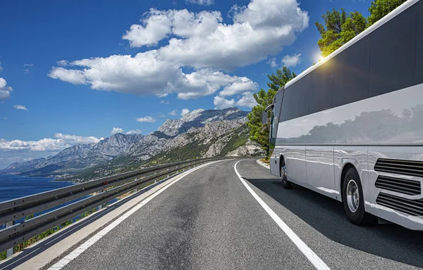 A white tourist bus rides along the highway against the backdrop of a beautiful sea landscape.