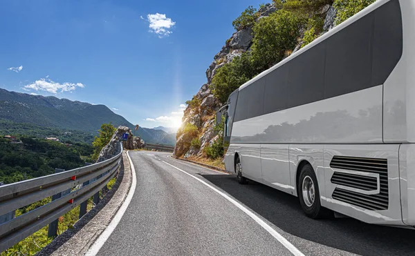 A white tourist bus rides along the highway against the backdrop of a beautiful landscape.