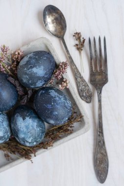 Mavi Paskalya yumurtaları, beyaz ahşap masa üzerinde paskalya yumurtaları kuru çiçekler, çatal ve kaşık.