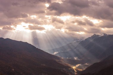 Rusya, Krasnodar Bölgesi. Soçi. Rosa Khutor Dağı Tatil Köyü. Güneşin ışınları sabah ve öğleden sonra bulutların arasından dağların zirvelerine çıkıyor..