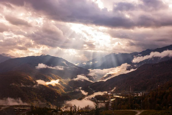 Rusya, Krasnodar Bölgesi. Soçi. Rosa Khutor Dağı Tatil Köyü. Güneşin ışınları sabah ve öğleden sonra bulutların arasından dağların zirvelerine çıkıyor..
