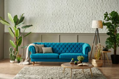 Kahverengi klasik şebeke ve beyaz tuğla duvarın önündeki mavi örtülü kanepe, yeşil bitki lambası dizaynından battaniye vazosu, saat tasarımı.