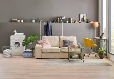 Gri duvardaki çamaşır ve kurutma makinesi arka plan, çamaşır, giysi, kanepe ve çalışma masası tarzı, minimalist iç mekan..