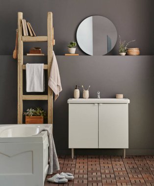 Modern banyo odası dolabı, lavabo, ayna ve küvet tarzı gri duvar fonu, vazo, bitki, çamaşır, havlu ve ahşap merdiven süslemeleri..