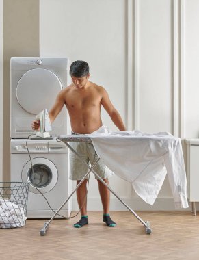 Adam banyoda ütü yapıyor, çamaşır ve kurutma makinesi beyaz ve kahverengi duvarların önünde..