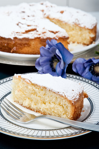 One plate with a slice of an apple cake with the big cake on the background. Flowers like freshness of the cake.